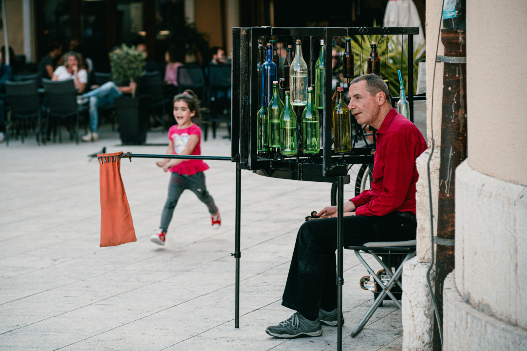 Ljetna atmosfera ispred kazališta uz uličnog svirača koji svira boce